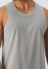 Graues ärmelloses Sporttop aus weichem, strukturiertem Stoff. Mit einem dezenten Nike-Logo auf der Brust. V-Ausschnitt-Design.