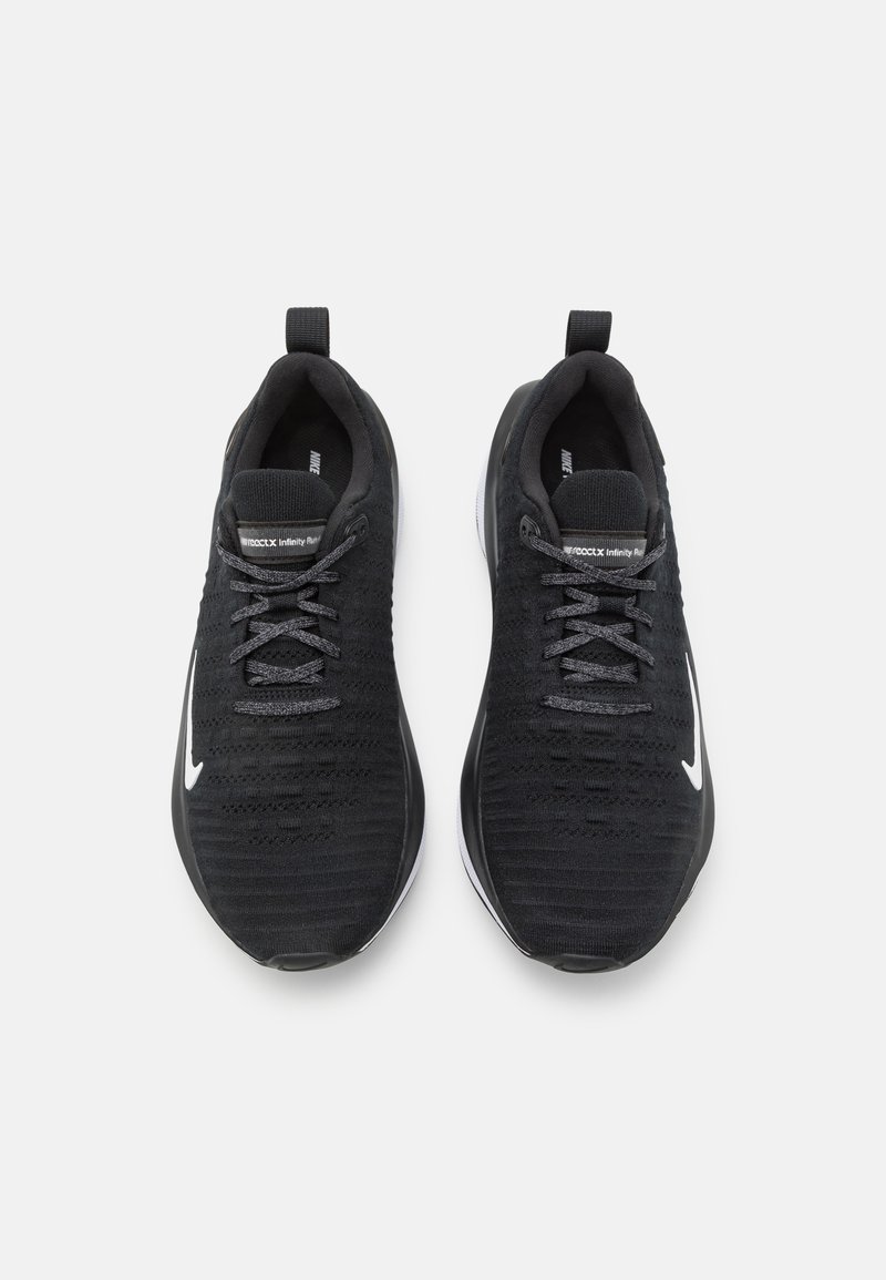 Zapatillas deportivas negras con una parte superior texturizada y tejida, logo de swoosh blanco en contraste y cordones grises. Diseño ligero con una suela acolchada.