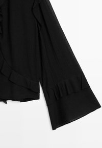 Haut noir à manches longues avec poignets larges et détails subtils de volants le long de la manche et de la couture latérale.