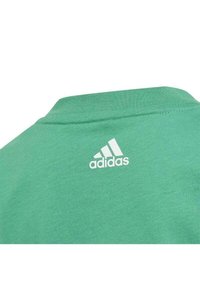 T-shirt verde in cotone con scollatura a girocollo. Presenta un logo bianco Adidas sul retro, che mostra una texture liscia e uniforme.