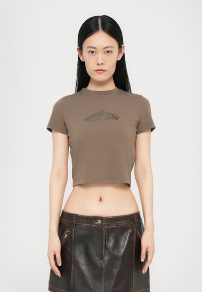 T-shirt court marron à manches courtes et encolure ronde, avec un imprimé logo subtil sur la poitrine ; associé à une jupe en cuir noire.