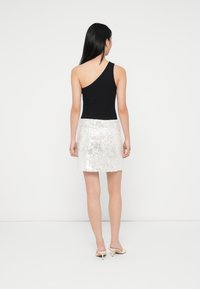 Black one-shoulder top paired with a short, sequined white skirt, featuring a textured surface and shimmering accents.