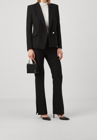 Černý dobře padnoucí blazer s vystouplými rameny, doplněný o elegantní černé kalhoty s postranními rozparky. Doplněno malou černou kabelkou.