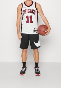 Biała koszulka koszykarska Chicago Bulls z czerwonymi akcentami, numer 11. Czarne szorty z białym logo Nike. Zawodnik trzymający piłkę do koszykówki.