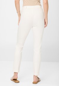 Pantalons blancs ajustés avec une texture lisse, une taille cintrée et une coupe à la cheville. Portés avec des sandales plates, montrant les pieds nus.