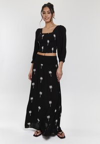 Svart tvådelad outfit som består av en kortärmad topp med puffärmar och palmträdbroderi, tillsammans med en lång, flödande kjol med matchande detaljer.