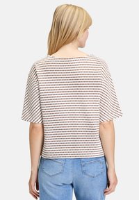Kortærmet top i hvid med brune prikker. Boxy pasform, rund halsudskæring, struktureret materiale og lige kant. Kombineret med blå jeans.