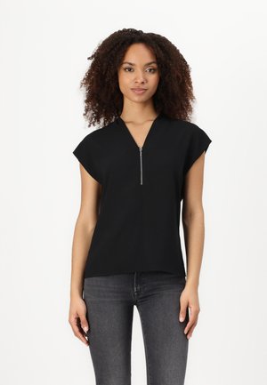 Schwarzes Kurzarmoberteil mit V-Ausschnitt und vorderem Reißverschluss. Glattes Material, entspannter Schnitt und minimalistisches Design. Kombiniert mit dunklen Jeans.