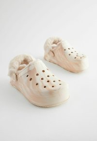 Zoccoli foderati in pelliccia sintetica con un motivo marmorizzato in rosa chiaro e crema, dotati di fori di ventilazione e una suola piatta leggera.