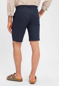 Marineblaue Shorts aus leichtem Material mit lockerer Passform, zwei Gesäßtaschen und einem schlichten Saum. Getragen mit beigen Slipper-Sandalen.