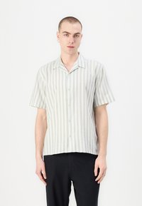 Īsām piedurknēm, ar apkakli, krekls gaiši zaļā un baltā vertikālā svītrā, ar pogu priekšpusi un brīvu piegriezumu. Gluda, viegla auduma.