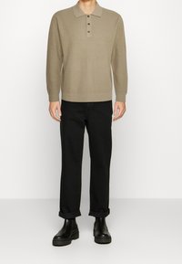 Polo beige a maniche lunghe in maglia con tre bottoni al colletto. Abbinato a pantaloni neri con risvolto e stivali neri chunky.