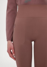 High-waisted, form-fitting leggings in a muted brown color, featuring a smooth texture and a discreet side zipper pocket.
