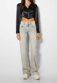 Svart satin cropped långärmad skjorta kombinerad med ljusuvaskade rakbenbyxor och vita sneakers. Notabel knappdetalj på skjortan.