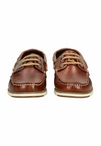Brune læderbådsko med hvide gummisåler, der har en moccasin-tå, dekorativ syning og kontrasterende beige snørebånd.