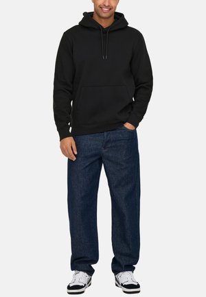 Black hooded sweatshirt with a front pocket, paired with loose-fit dark blue denim jeans and white sneakers with black accents.