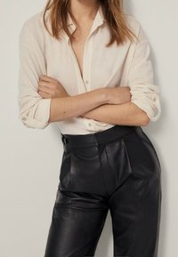 Light beige button-up shirt with rolled sleeves, paired with high-waisted black leather trousers featuring front pleats. Minimalistic design.