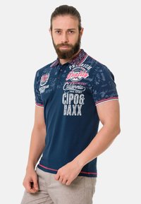 Navyblaues Poloshirt mit grafischen Drucken in Weiß und Rot. Verfügt über einen kontrastierenden gemusterten Kragen und kurze Ärmel mit roten Stichakzenten.
