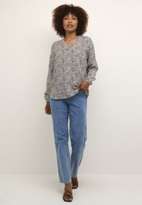 Schwarz-weiß gemusterte Bluse mit V-Ausschnitt und langen Ärmeln, kombiniert mit hellblauen Jeans und schwarzen Riemchenschuhen.