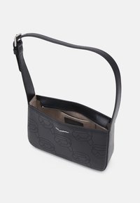 Sac à épaule noir avec motif perforé, logo argenté, sangle ajustable et fermeture éclair partiellement ouverte révélant une doublure intérieure beige.