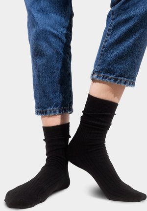 Czarne prążkowane bawełniane skarpetki sięgające ponad kostkę, zestawione z krótkimi niebieskimi jeansami z postrzępionymi krawędziami.