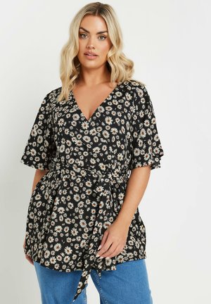Haut en fleur noir à manches courtes, orné de marguerites blanches et d'accent orange. Tissu léger avec une taille nouée pour donner de la forme.