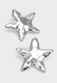 Orecchini a forma di stella argentata con una superficie liscia e riflettente e cinque punte, che mostrano una finitura metallica lucida e una leggera curvatura.