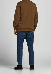 Sudadera marrón de corte relajado, vaqueros de mezclilla azul y zapatos negros. Textura suave, diseño sencillo y detalles de bolsillos estándar en los vaqueros.