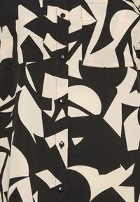 Chemise à manches courtes en tissu lisse présentant un motif abstrait audacieux noir et crème, avec un devant à boutons et une poche poitrine.