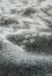 Tessuto di lana grigio e bianco con una superficie morbida e pelosa e leggere variazioni nel motivo, che scende delicatamente con un aspetto ondulato.