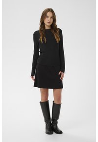 Fekete hosszú ujjú felső fekete szoknyával párosítva, sima textúrával. Az összeállítást magas fekete csizmák egészítik ki, harmonikus megjelenést teremtve.