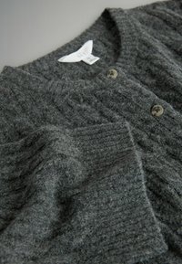 Šedý pletený cardigan s žebrovanou texturou, kulatým výstřihem a dvěma knoflíkovými uzávěry. Měkká tkanina s mírně chmýřitou strukturou.