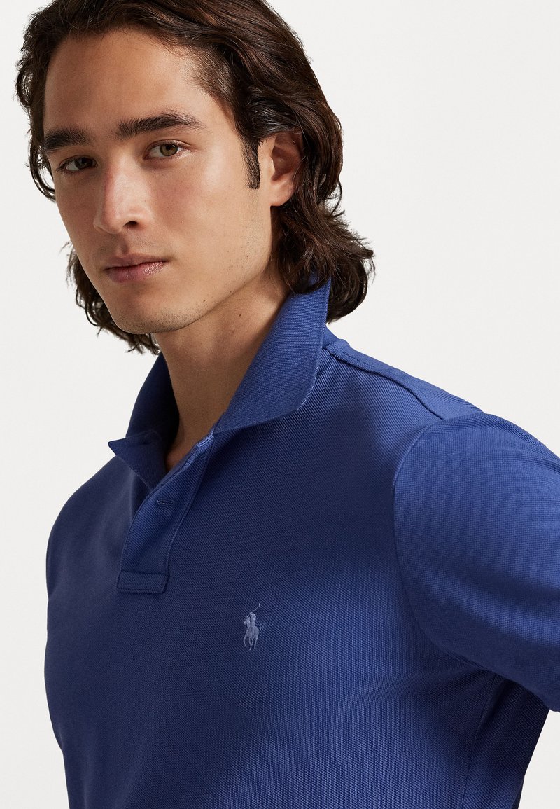 Blauwe polo shirt van een gestructureerde stof, met een opgestroopte kraag en een klein, geborduurd logo op de borst.