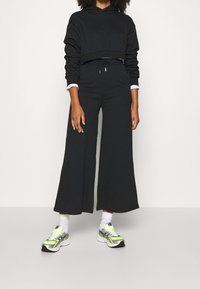 Czarna skrócona bluza z długim rękawem w połączeniu z szerokimi czarnymi spodniami. Buty są białe z neongółowymi i srebrnymi akcentami.