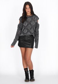 Zwart en grijs gebreid sweater met uitsparingen op de schouders, gecombineerd met een zwarte leren minirok en zwarte veterschoenen.