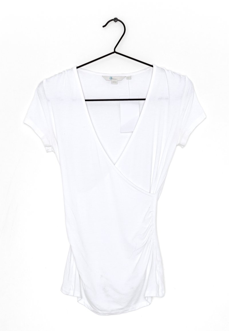 Blouse blanche à manches courtes avec col en V sur un cintre noir sur fond blanc.