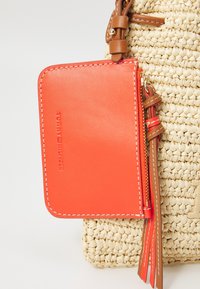 Tommy Hilfiger kortti-/rahakotelo kirkasta oranssia nahkaa, jossa on valkoiset ompeleet ja vetoketjusuljenta. Kiinnitetty teksturoidun olkakassin kanssa, jossa on ruskeita yksityiskohtia.