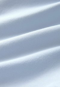 Biela látka s hladkou textúrou, ktorá zobrazuje jemné vlnky a záhyby. Materiál pôsobí mäkko a ľahko, vhodný na oblečenie alebo čalúnenie.