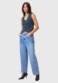 Marinblå ärmlös topp med v-ringning och knapprad, i kombination med vida ljusdenimjeans med fransade fållar och svarta ankelstövlar.