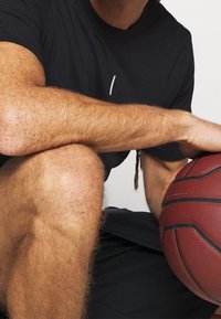 Černé sportovní tričko s kulatým výstřihem, se základním bílým liniovým grafickým designem, doplněné basketbalem a černými šortkami.