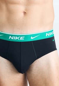Schwarze Unterhosen mit einem grün-weißen Nike-Logo-Bund. Hergestellt aus einem glatten Stoff mit einer taillierten Passform und sichtbaren Nahtdetails.