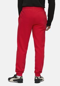 Røde sweatpants med elastisk talje, sidelommer og tapered ben. Båret med sorte sportsko med en beige detalje.