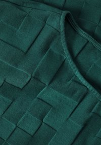 Tela verde texturizada con un patrón tejido de parches elevados; acabado liso y textura suave; escote curvado con bordes cosidos.