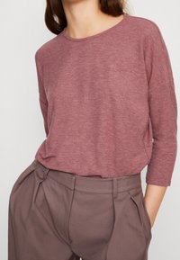Maglione a maniche lunghe color marrone in un tessuto morbido e texturizzato, abbinato a pantaloni marroni a vita alta con pieghe. Silhouette casual e ampia.