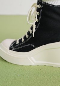 Černé vysoké tenisky z plátna s bílým kontrastním prošíváním, kulatou špičkou a silnou, strukturovanou bílou podrážkou. Obsahují béžové tkaničky.