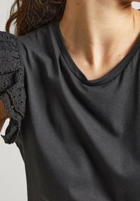 Czarny T-shirt z rękawami z żabotem z ażurowej tkaniny, zaokrąglonym dekoltem i gładką fakturą, z widocznymi szwami i lekkim układem.