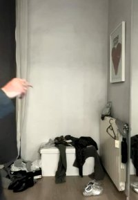 Ακατάστατη γωνία με ρούχα στοιβαγμένα σε ένα λευκό πάγκο αποθήκευσης, παπούτσια στο πάτωμα, πλαίσιο με έργο τέχνης καρδιάς στον τοίχο και ένα καλοριφέρ με κρεμάστρα.