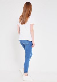 Vit T-shirt och blå skinny jeans, matchat med vita sneakers. Håret är rakt och långt. Utsikten är från baksidan.