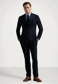 Marinblå randig dubbelfliks kostym med skräddarsydd passform, som kompletteras av en ljusblå skjorta och mörk slips. Bruna läderskor fulländar outfiten.