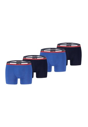 Männlicher Oberkörper trägt blaue Levi's Boxershorts mit weißem, rotem und marineblauem Markenbund und steht vor einfachem hellem Hintergrund.